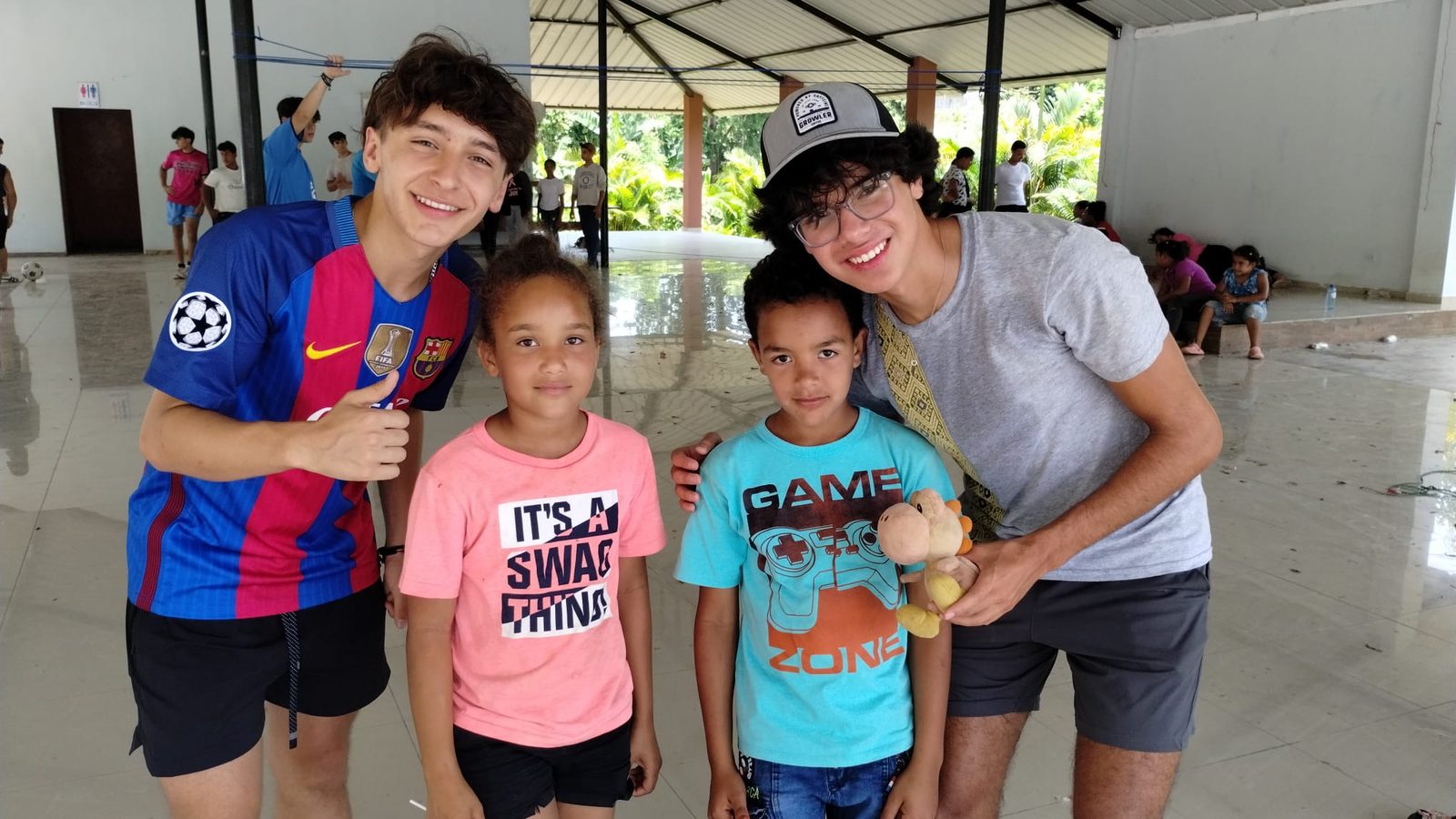 Mathi Abreu in a Barcelona jersey, smiling alongside two children and a friend during a service trip in the Dominican Republic